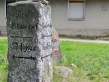 Wegweiserstein - im Hintergrund Gedenkstein und die alte Schmiede